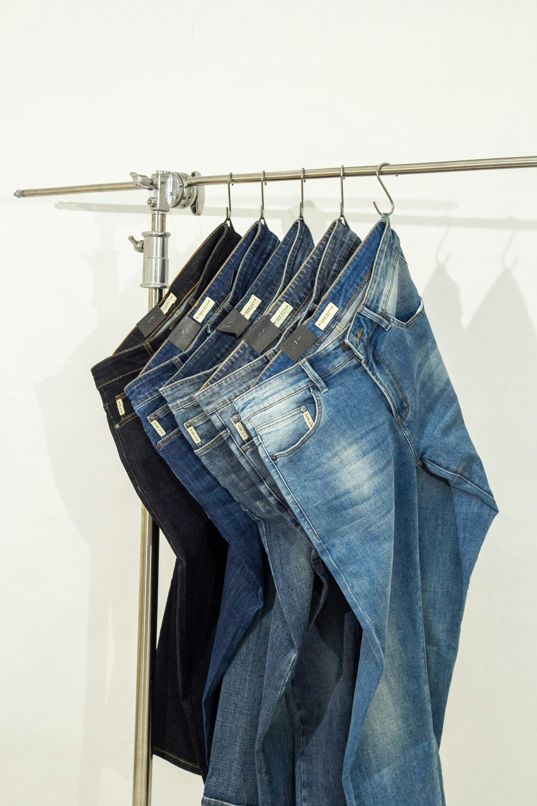 Several pairs of jeans in different washes hanging neatly on metal hangers on a clothing rack.