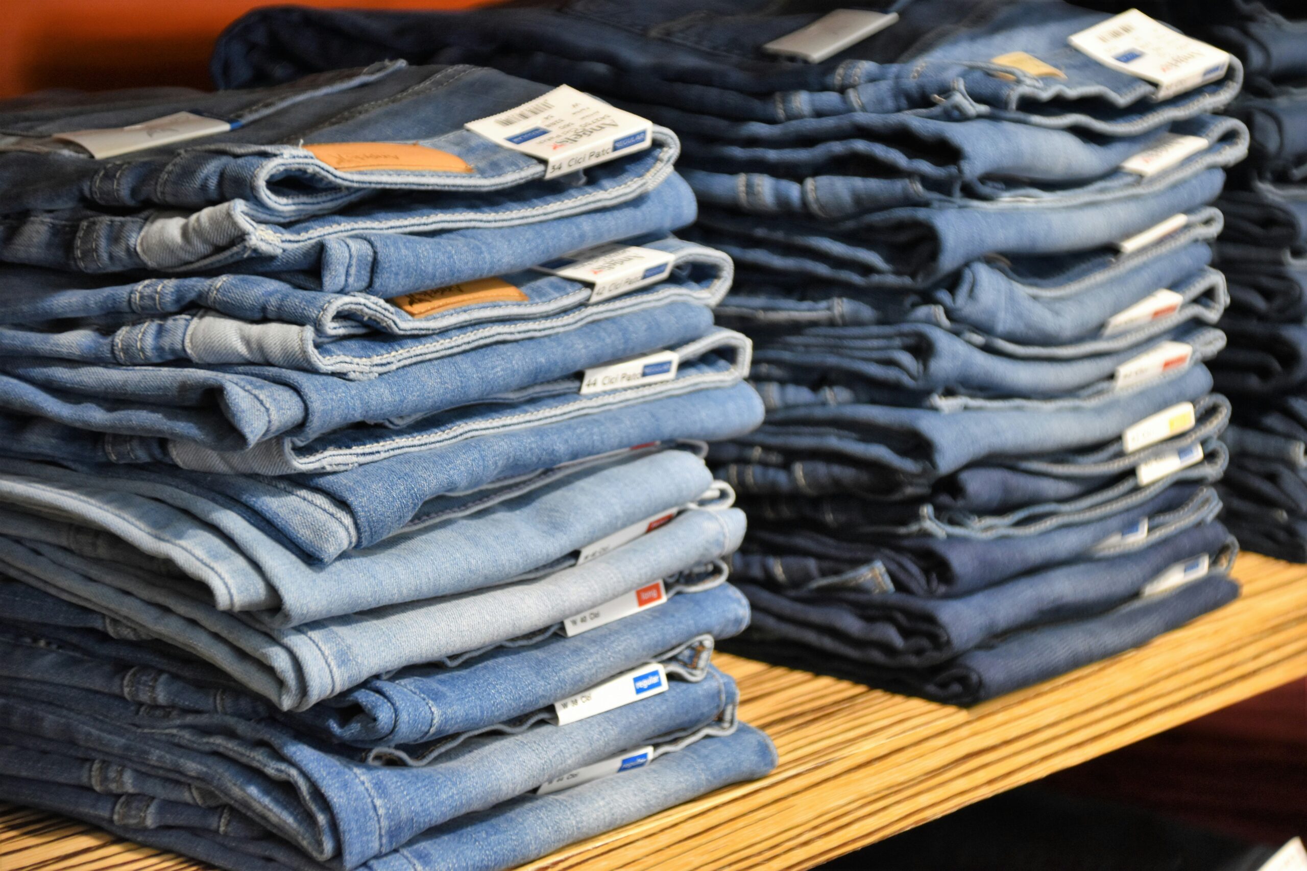 Multiple piles of folded jeans in various blue tones arranged on wooden shelves in a store.